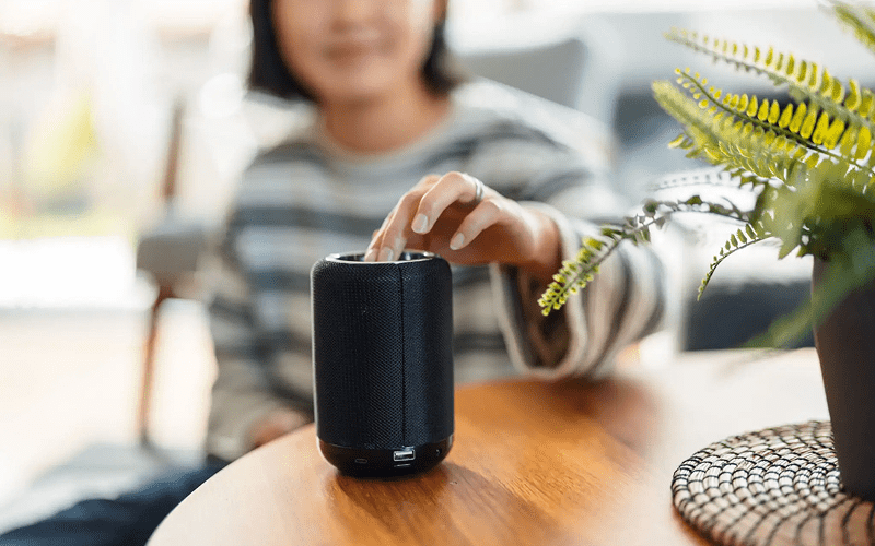 A person in a striped sweater gently interacts with a black smart speaker on a wooden table