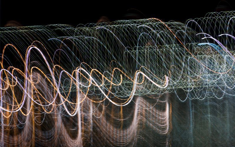 Abstract light trails creating wavy patterns against a dark background.